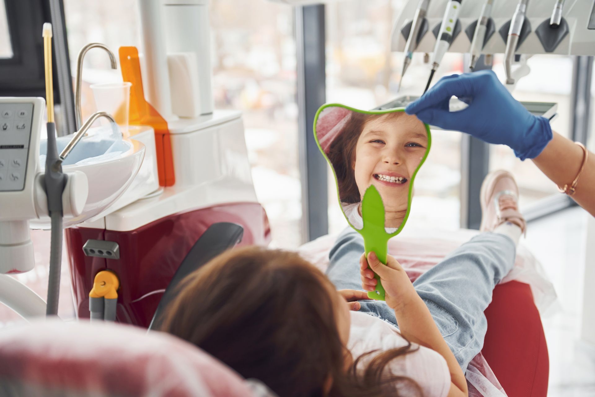 A little girl is looking at her teeth in a mirror at the dentist.