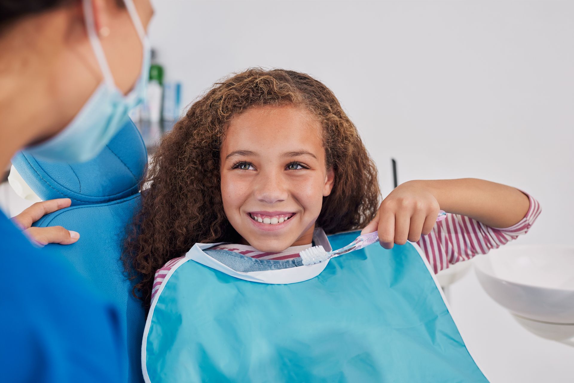 Girl smiling at dentist during a dental checkup, wearing a blue bib, in a dental office.