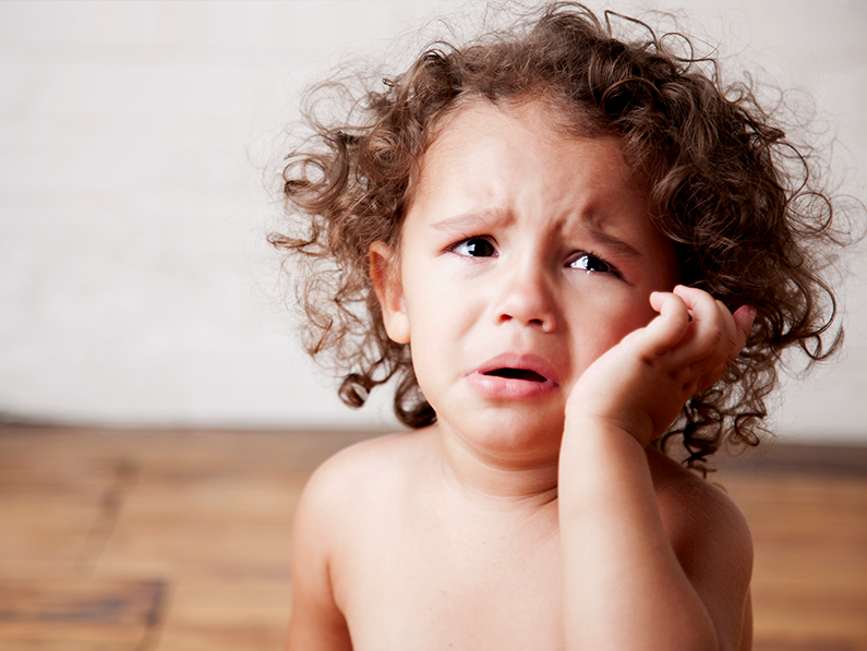 A little girl with curly hair is crying with her hand on her face.