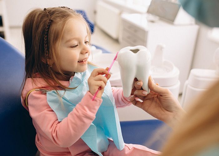 A little girl is brushing her teeth with a toothbrush in a dental office.