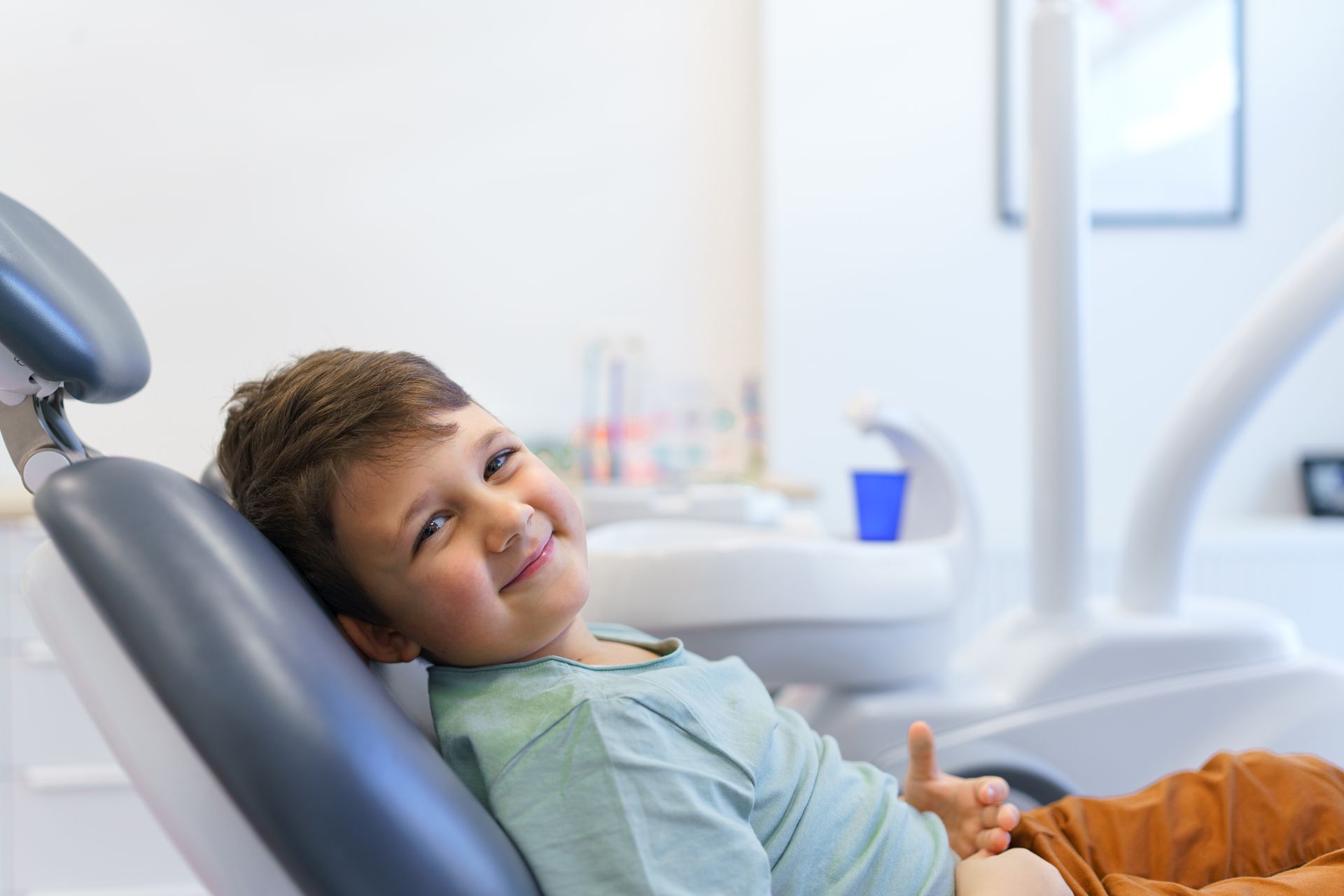 A young boy is sitting in a dental chair and smiling.