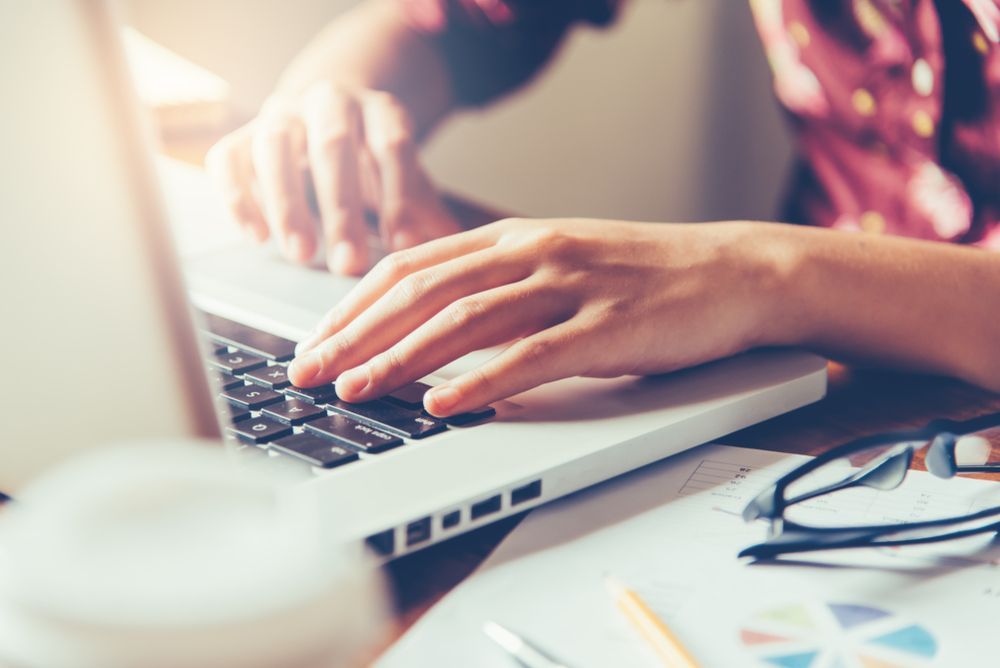 Person's Hands Typing on Laptop Keyboard; Desk With Papers, Glasses, and a Coffee Cup — Accountsloop Tax & Business Advisory in Geelong, VIC