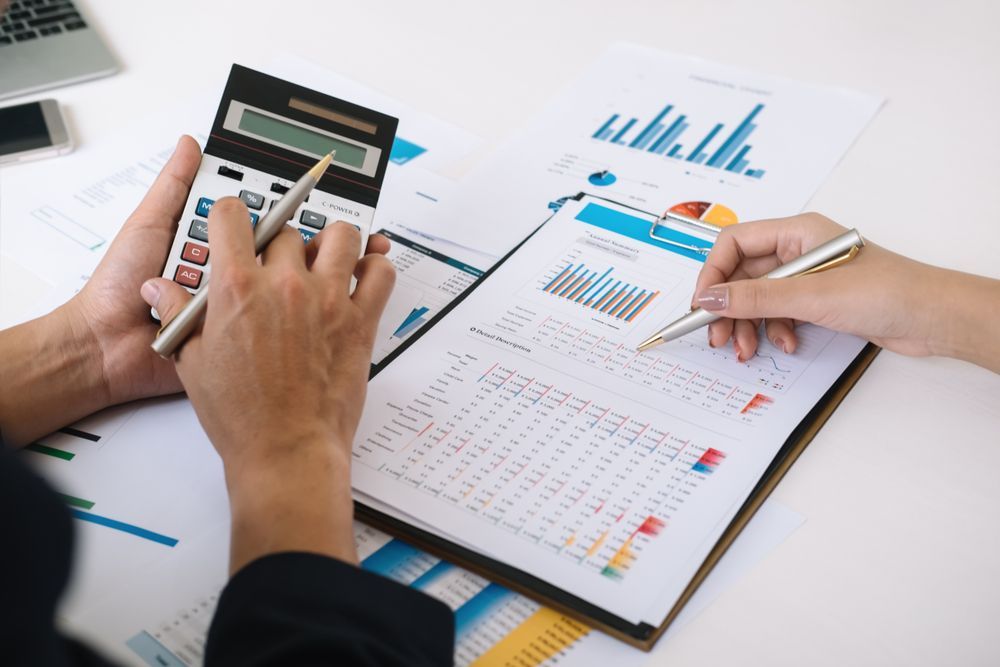 Two People Reviewing Financial Data With a Calculator and Pens, on a White Desk With Charts — Accountsloop Tax & Business Advisory in Geelong, VIC