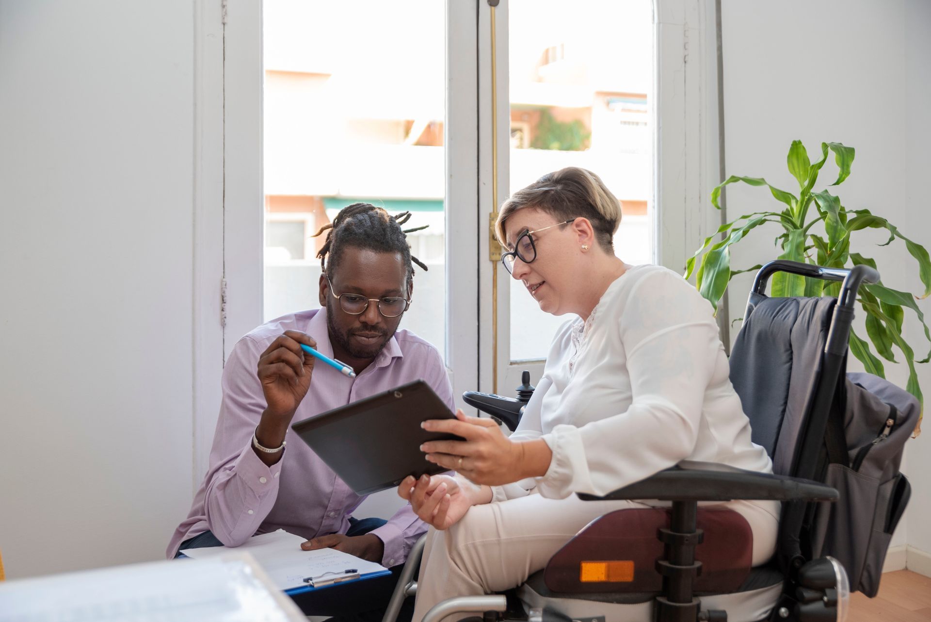 Man and Woman in Wheelchair Looking at Tablet, Discussing Documents in Office — Accountsloop Tax & Business Advisory in Geelong, VIC