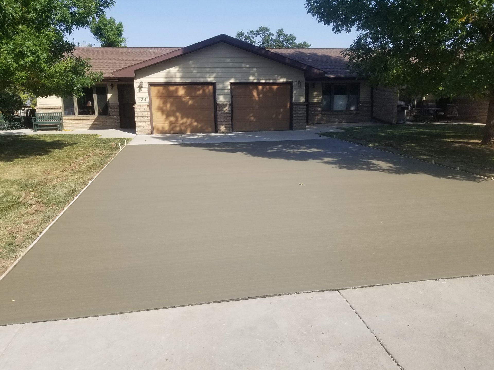 A concrete driveway leading to a house with a white fence
