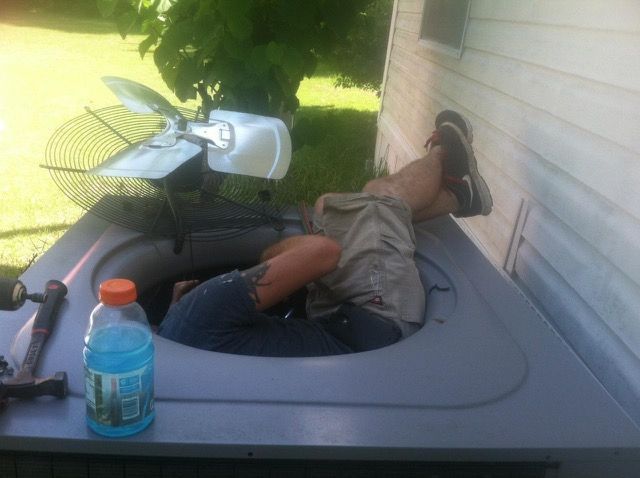 Person inside an air conditioning unit, working on it outdoors. A Gatorade bottle and tools sit nearby.