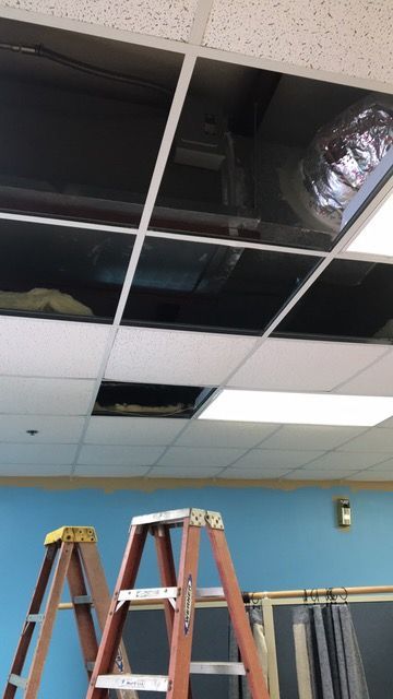 Ceiling tiles removed, exposing ductwork and wires; two ladders in front of a blue wall.