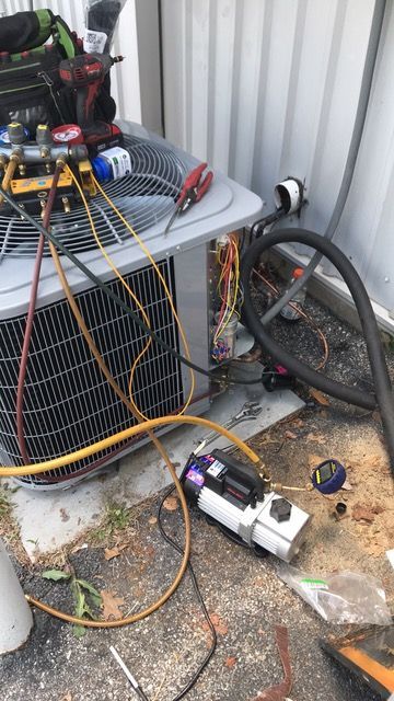 HVAC unit being serviced. Vacuum pump attached with gauges and hoses.  Various tools and wiring visible.