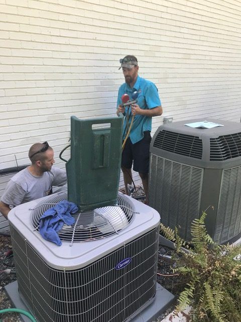 Two men servicing an air conditioning unit outside a building. One man uses a gauge.