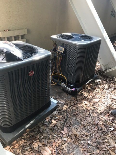 Two Rheem air conditioning units sit on pads, near a building.