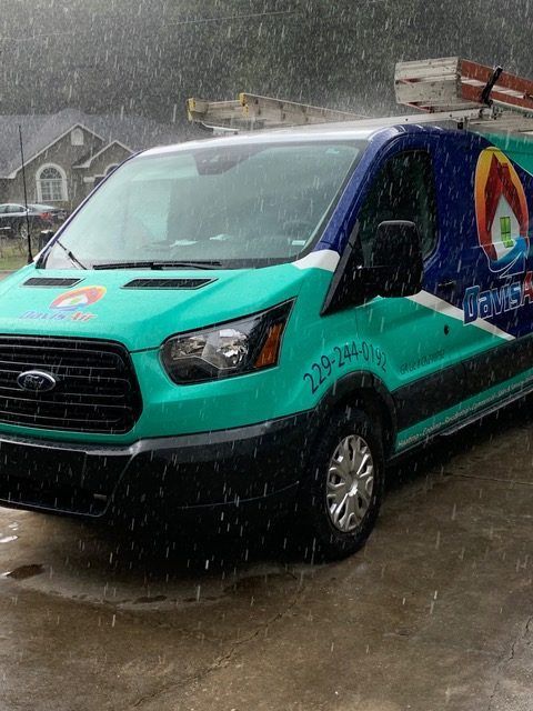 A teal and blue branded Ford van in the rain, parked in front of a house.
