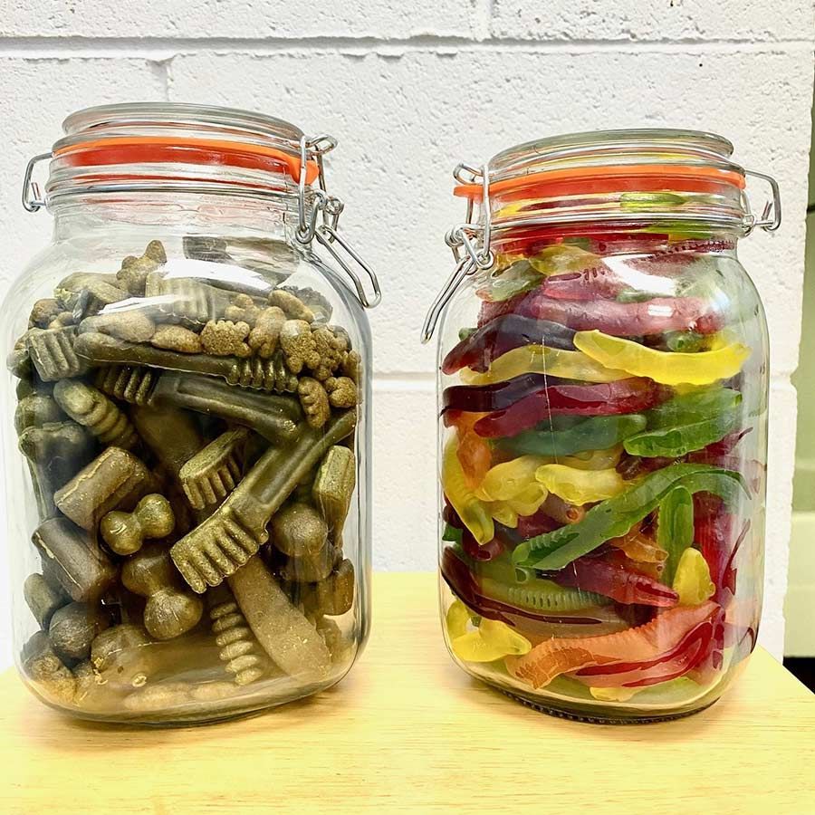 Two Jars of Dog Treats and Gummy Worms Are Sitting on a Wooden Table — Palms Vets–Hermit Park in Hermit Park, QLD