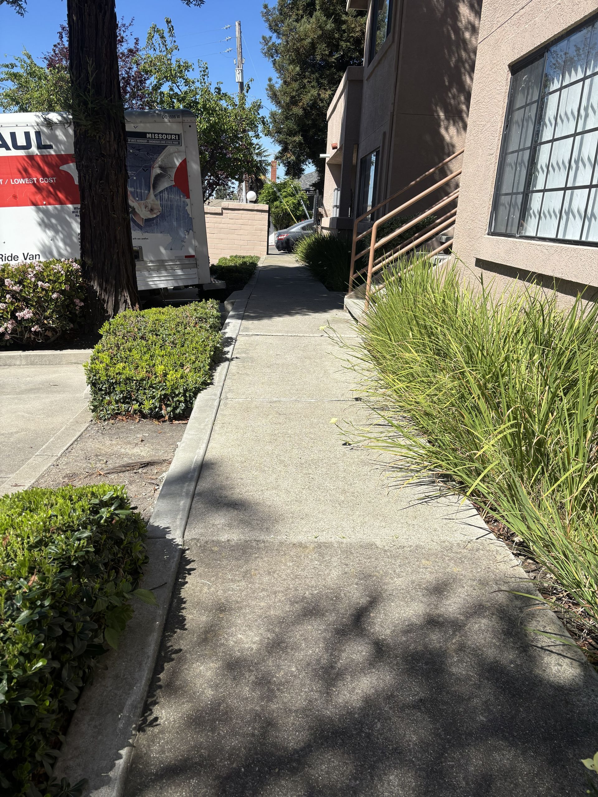 A paved walkway bordered by green bushes leads toward a building, with a U-Haul truck parked to the left.