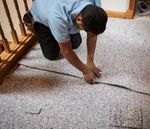 A man is kneeling down and cutting a piece of carpet