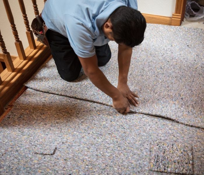 A man is kneeling down and cutting a piece of carpet