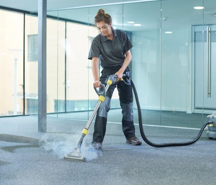 A woman is cleaning a carpet with a vacuum cleaner.