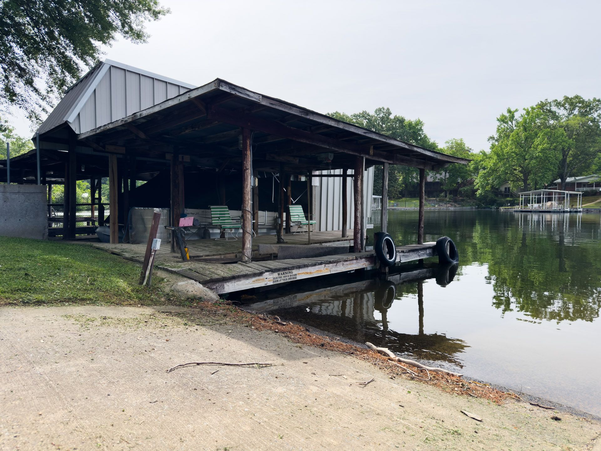Open lakeside boathouse with covered dock and boat lift beside calm water