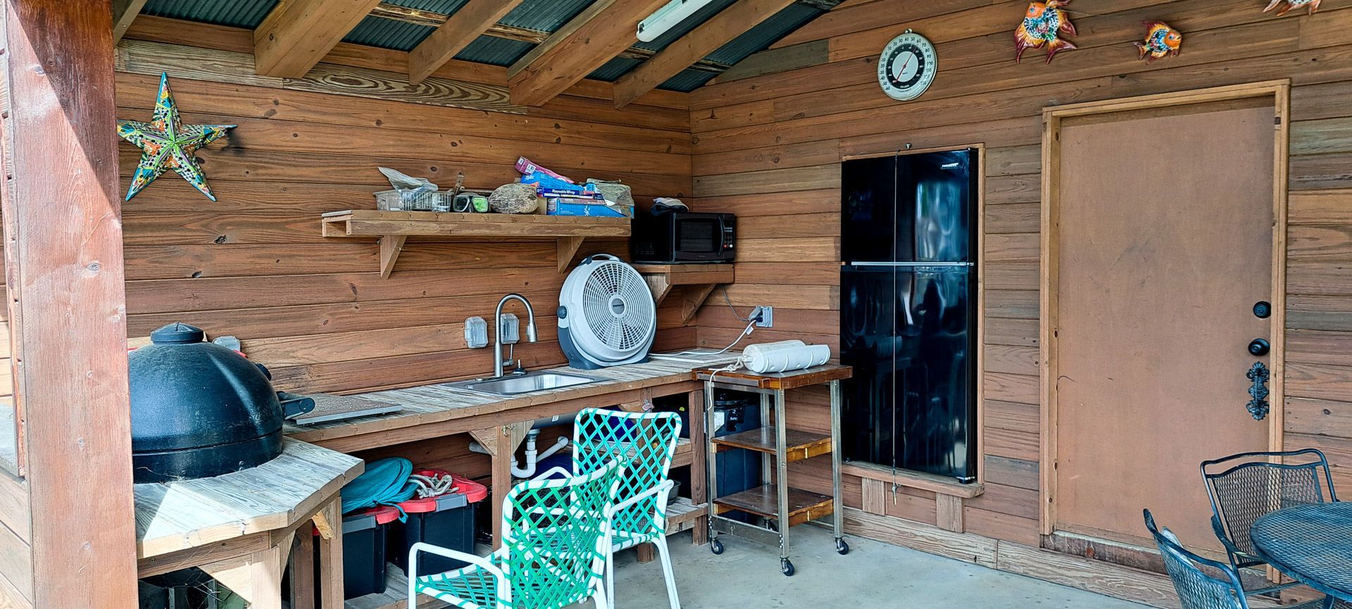Covered patio with brick wall, bar counter, stools, wood door, and a black refrigerator.