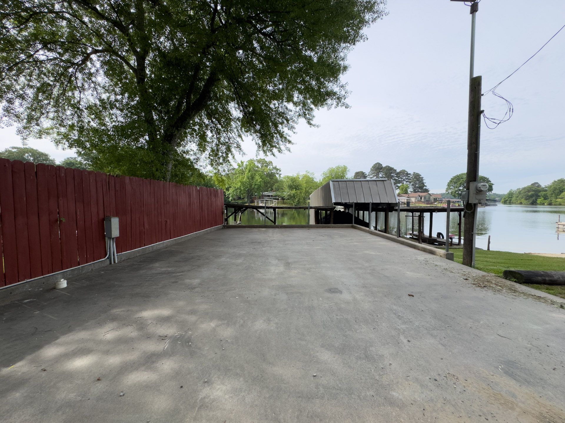 Empty paved road beside a red fence and lakeside dock under trees