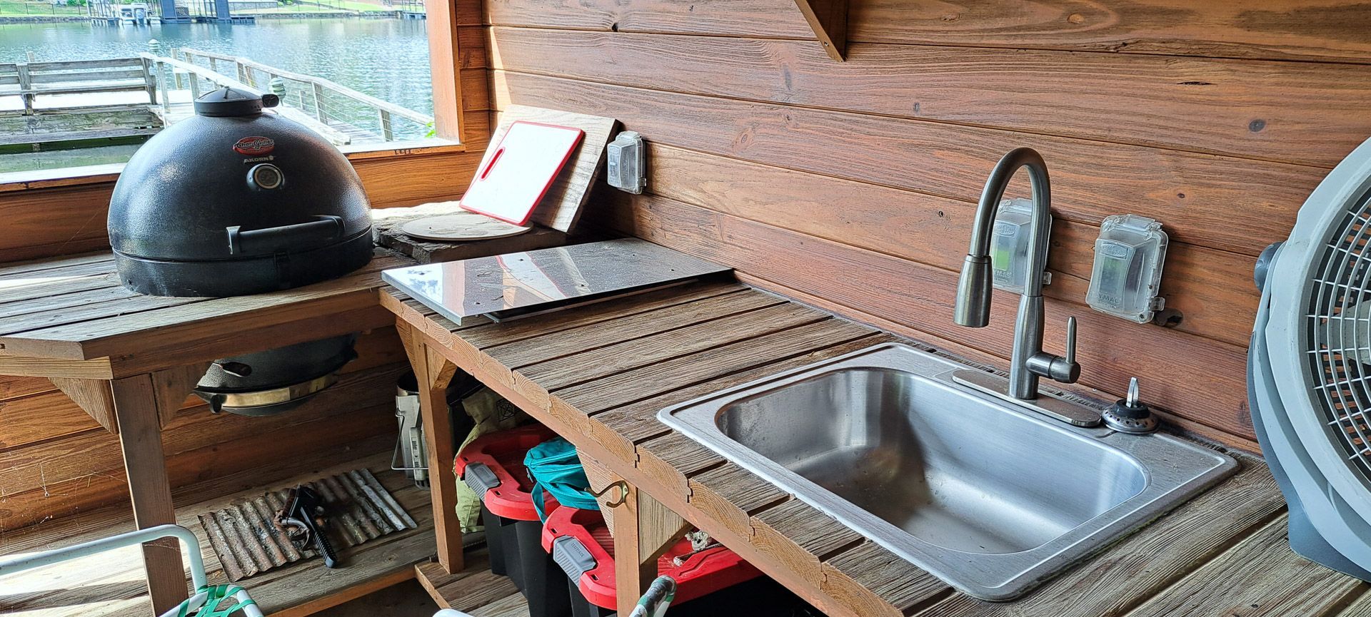 Wooden outdoor kitchen with grill, countertop, sink, and fan under a covered patio