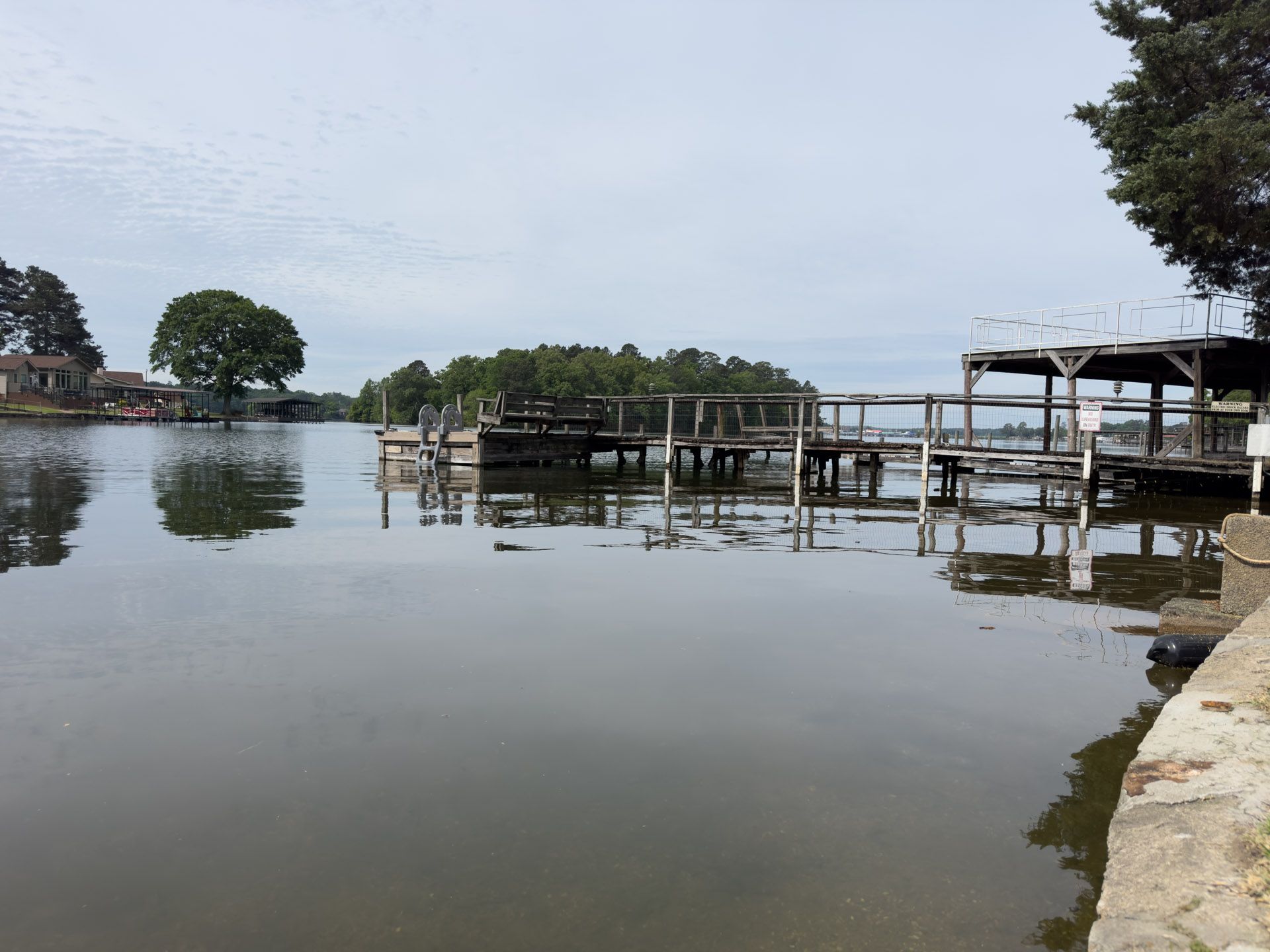 Calm lakeside with wooden docks, trees, and stone embankment under an overcast sky