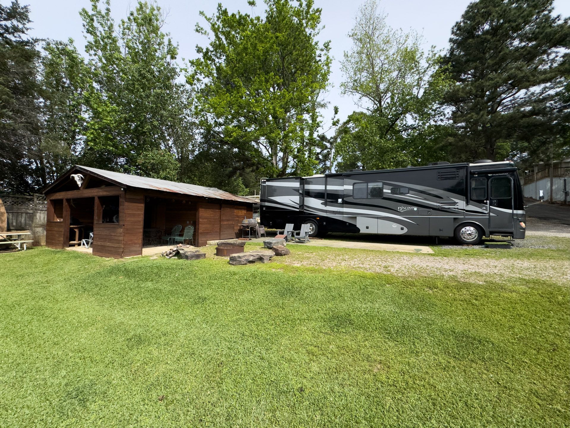 A brick cabin and a large black RV parked on a grassy yard with trees behind them.