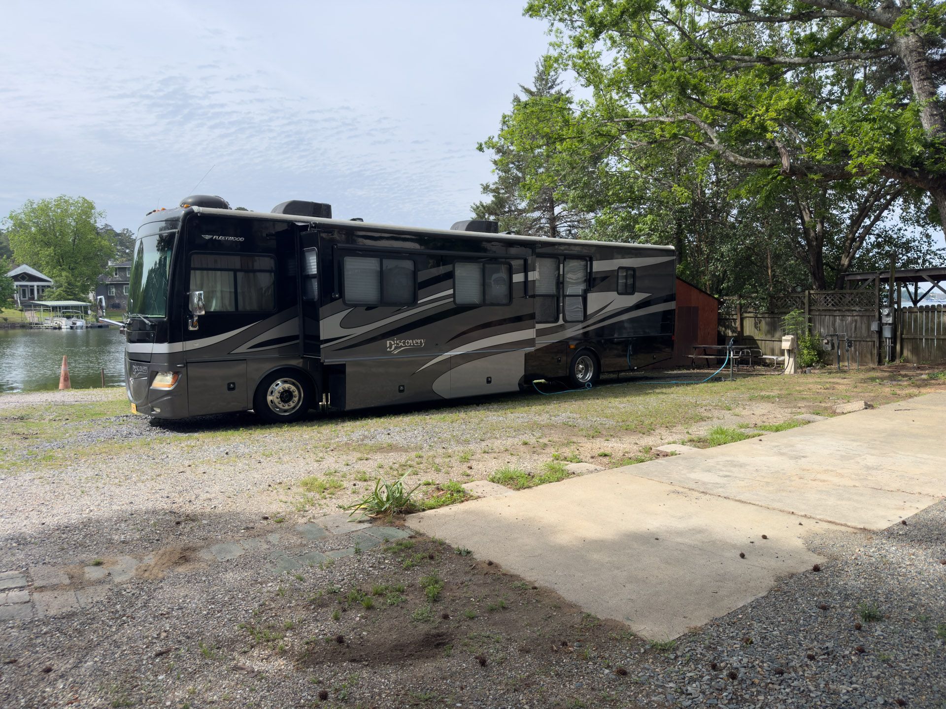 Large black and gray RV parked beside a lakeside path under trees.