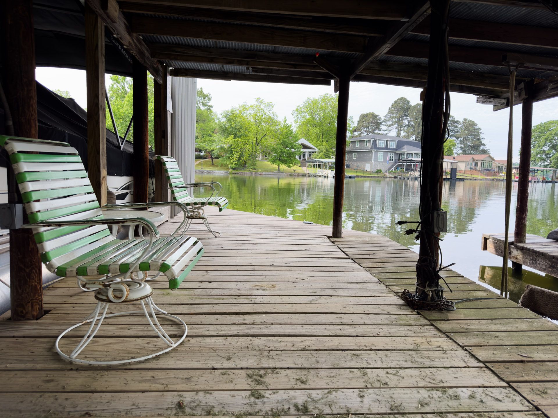 Covered wooden dock with striped bench chairs beside a calm lake and trees in the distance