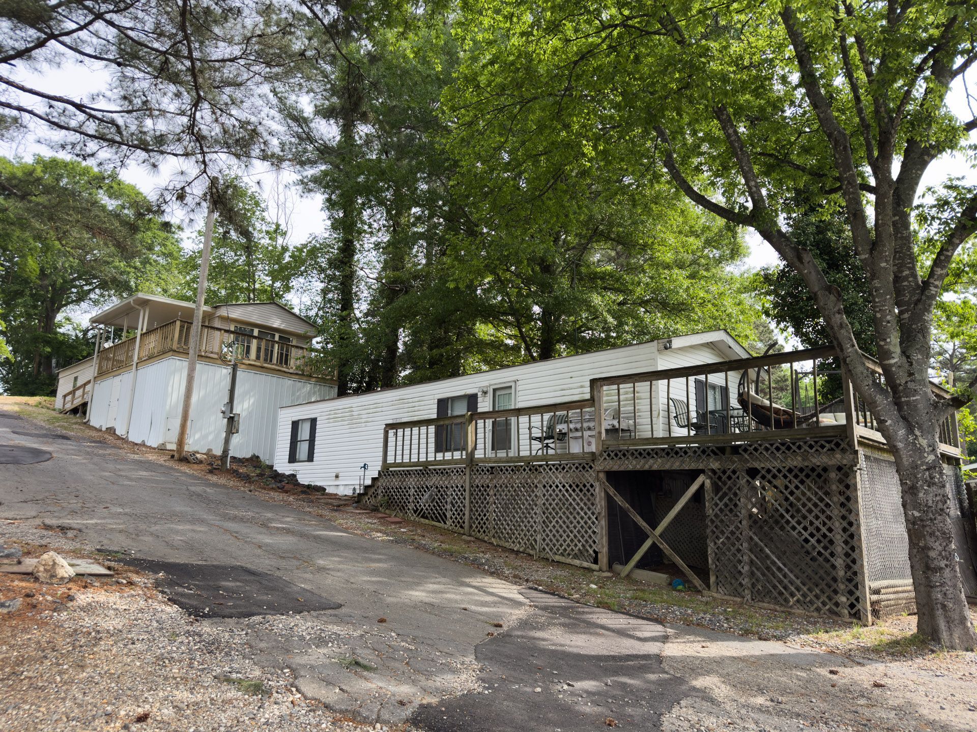 Hillside mobile homes and a deck along a wooded dirt road, with trees overhead