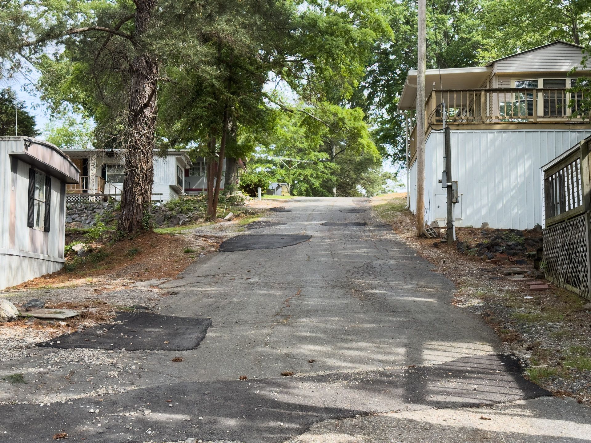 Steep driveway between trees and buildings, leading uphill on a sunny day