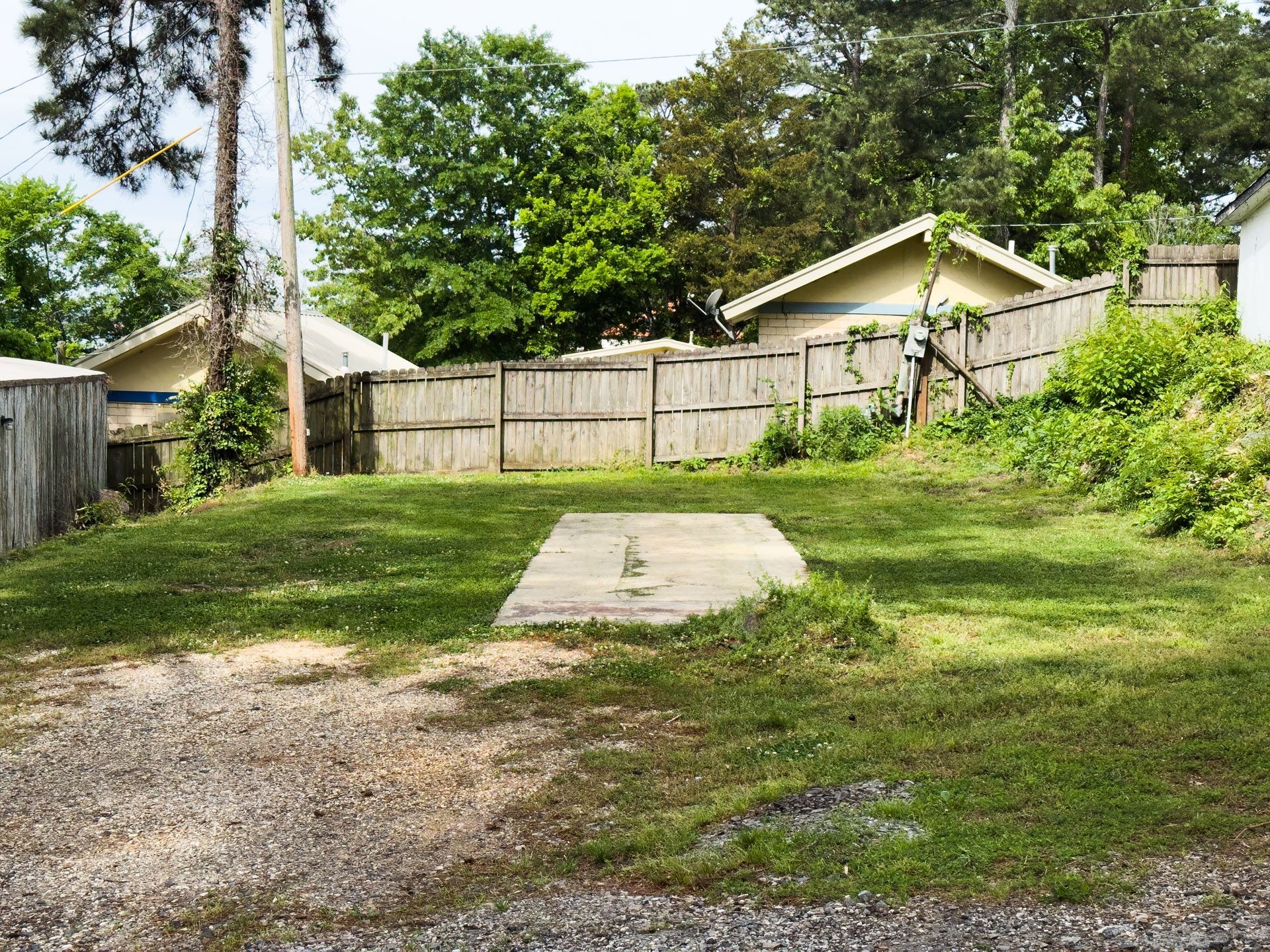 Backyard with a concrete slab, grassy ground, wooden fence, and trees behind houses