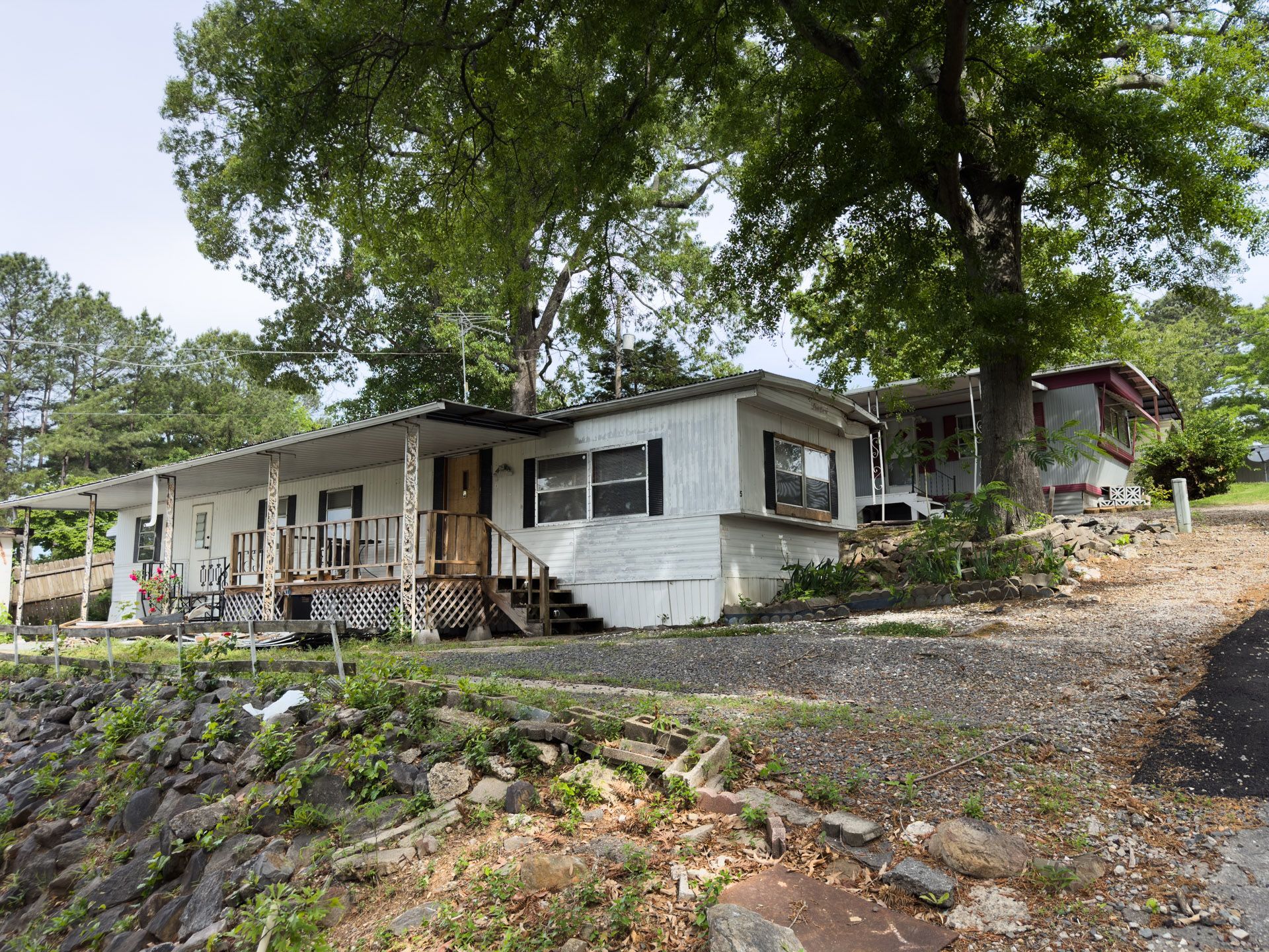 Single-story white house on a rocky hillside with large trees and a wooden porch