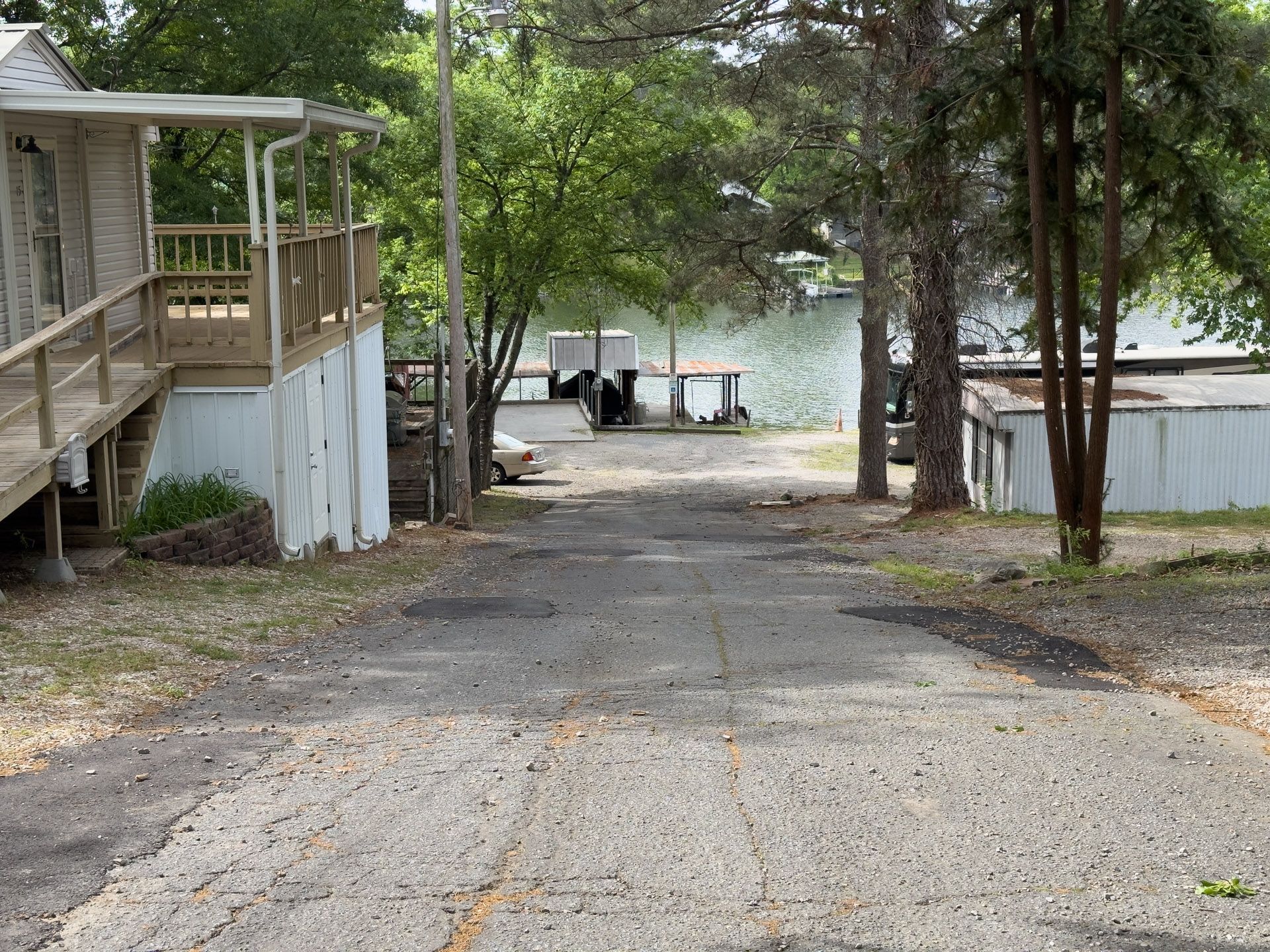 Gravel driveway leading to a lakeside dock, with trees and small cabins on either side.