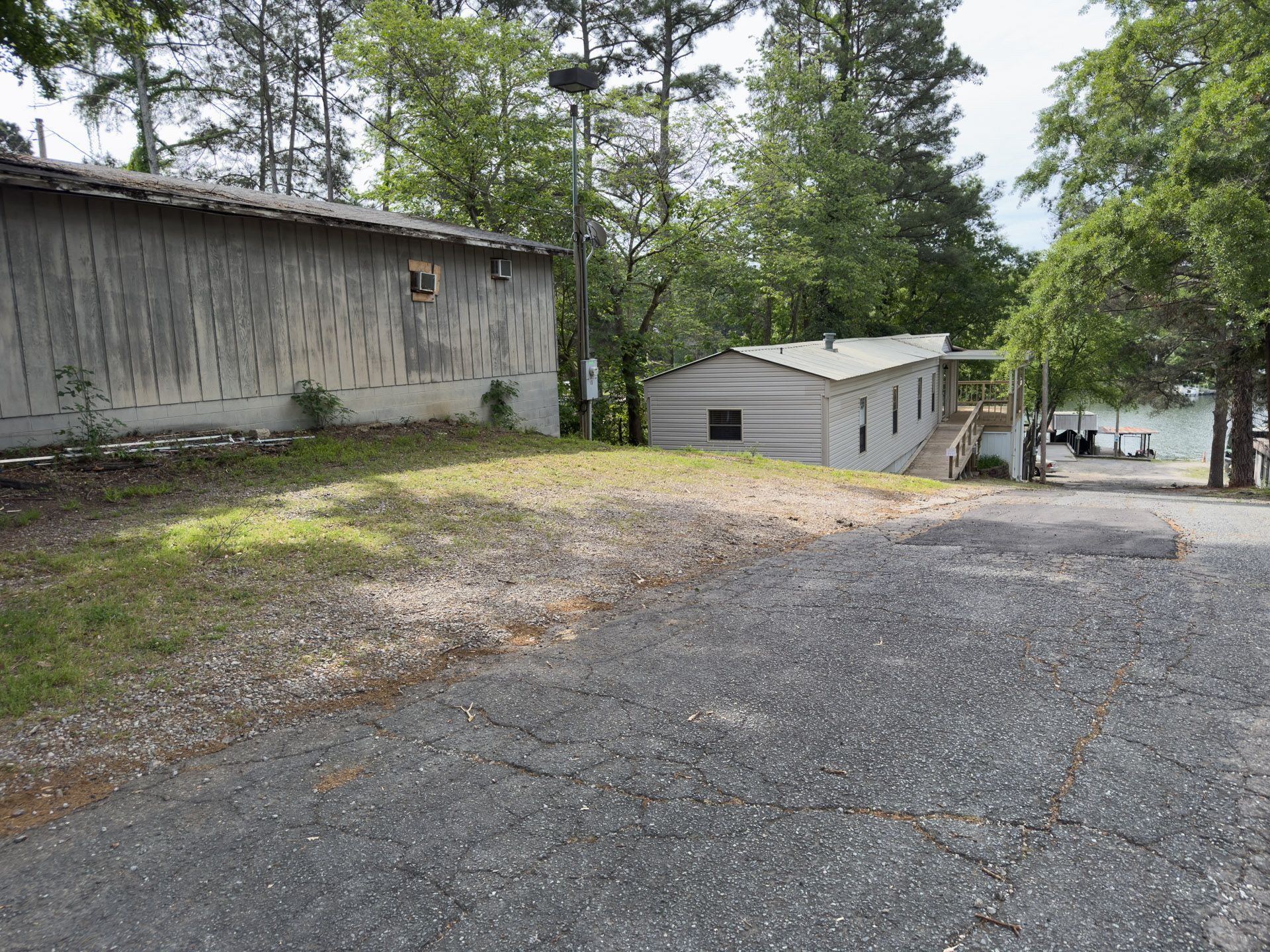 Gravel driveway beside weathered buildings and pine trees, leading down toward a lakeside dock
