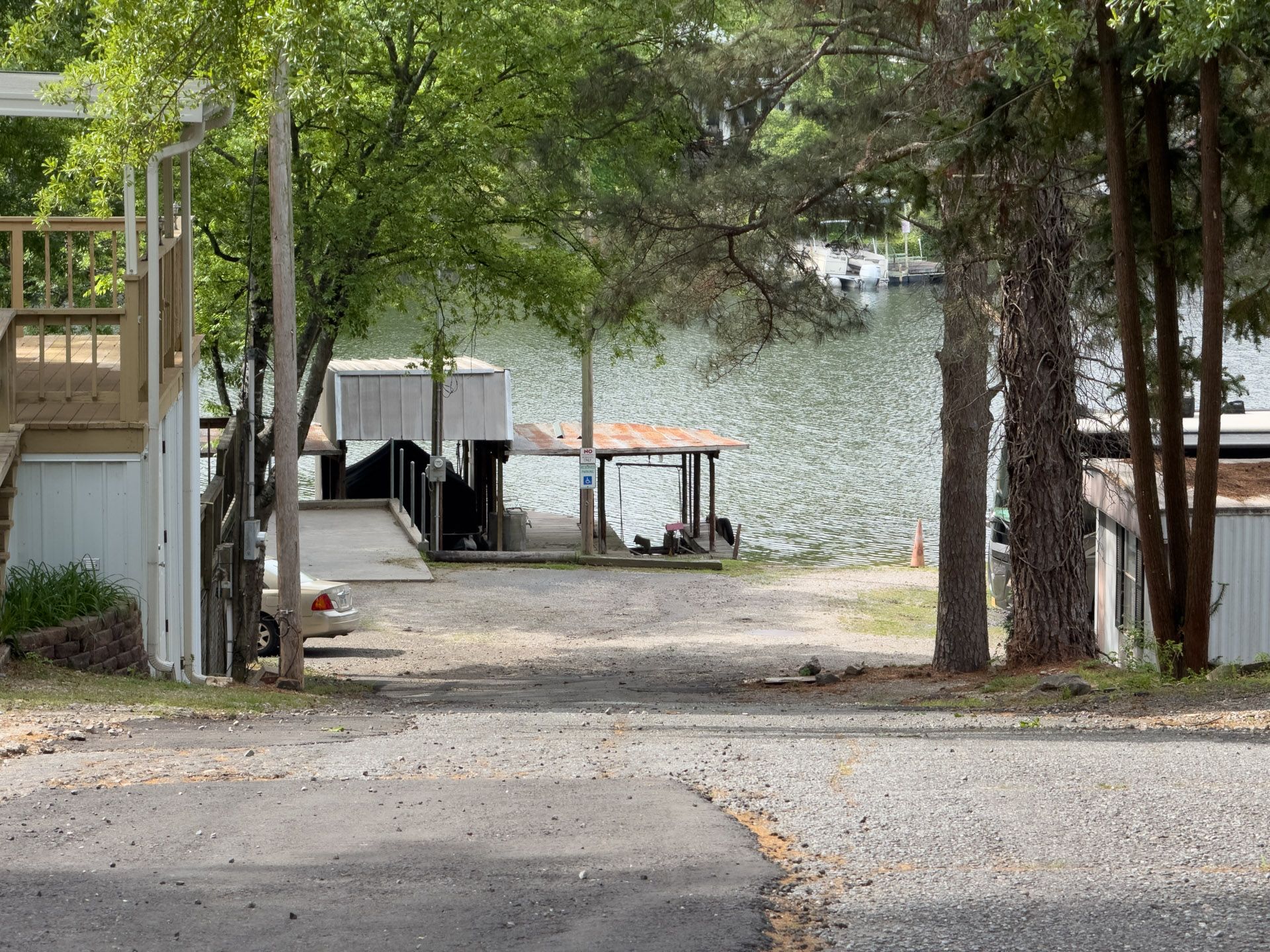 Driveway leading to a lakeside dock and boathouse, framed by trees and a house porch.