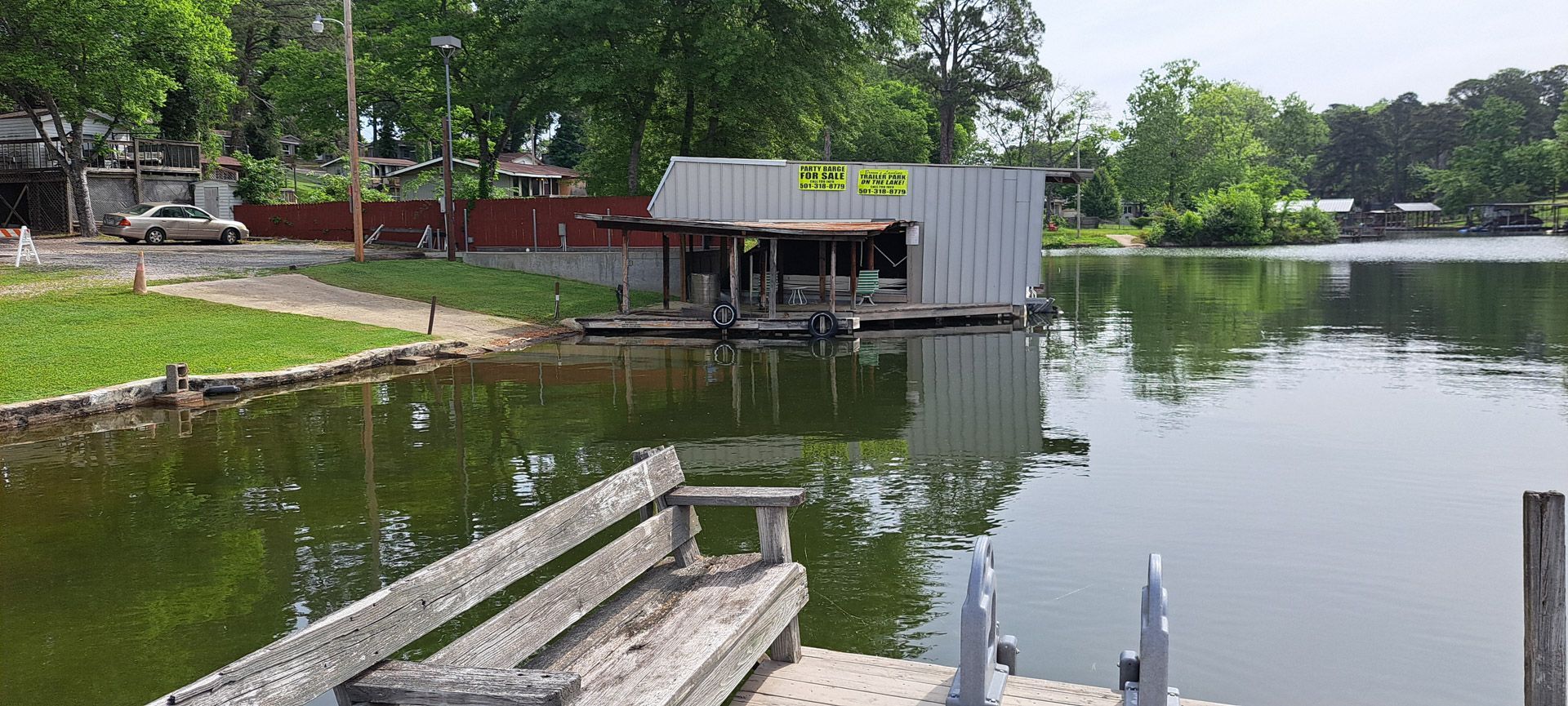 Calm lakeside dock with wooden bench, small boathouse, and green trees reflecting in the water