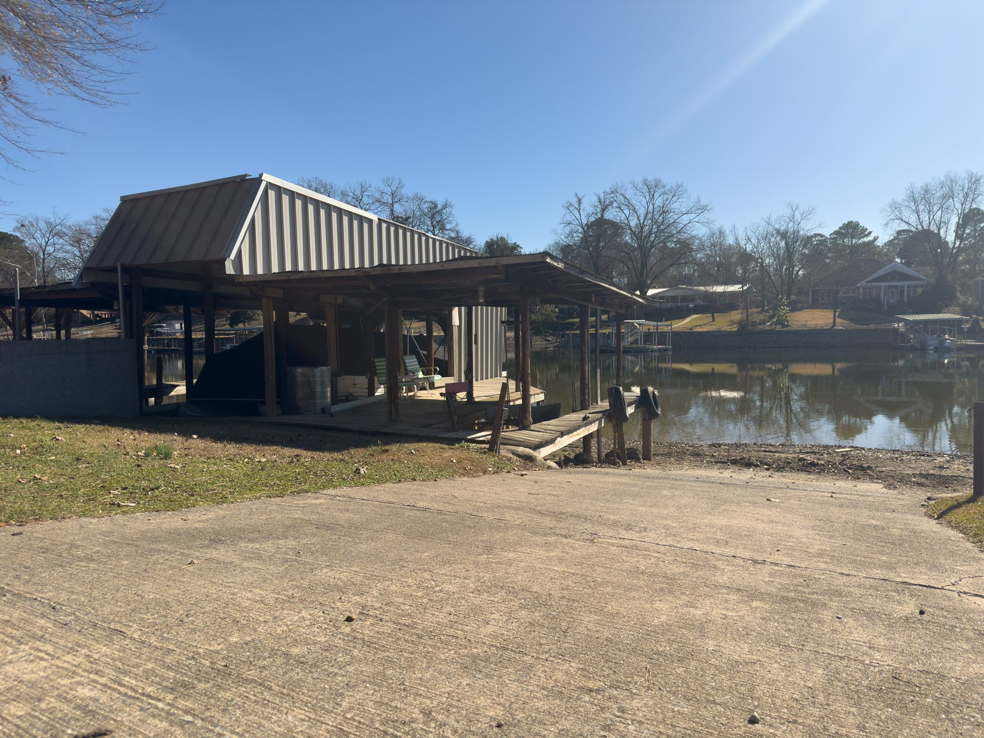 Boat ramp leading to a dock with a metal roof, next to a waterway with trees under a blue sky.