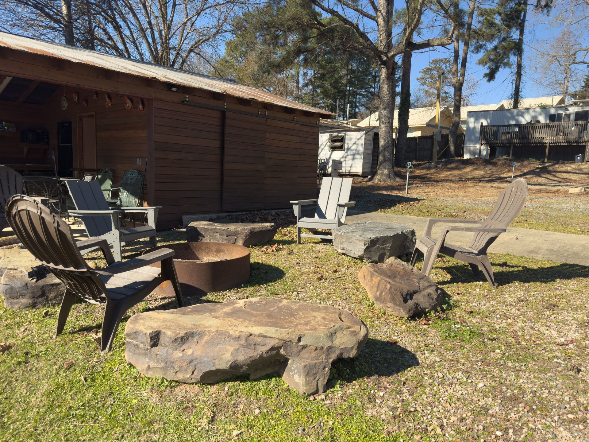 Outdoor seating area with chairs around a fire pit and a wooden building in the background.