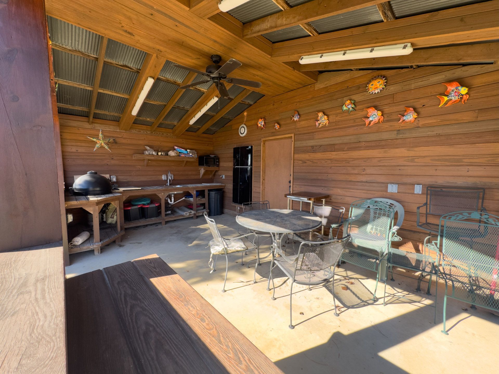 Outdoor kitchen with wood paneling, metal roof, table, chairs, and various decorations.