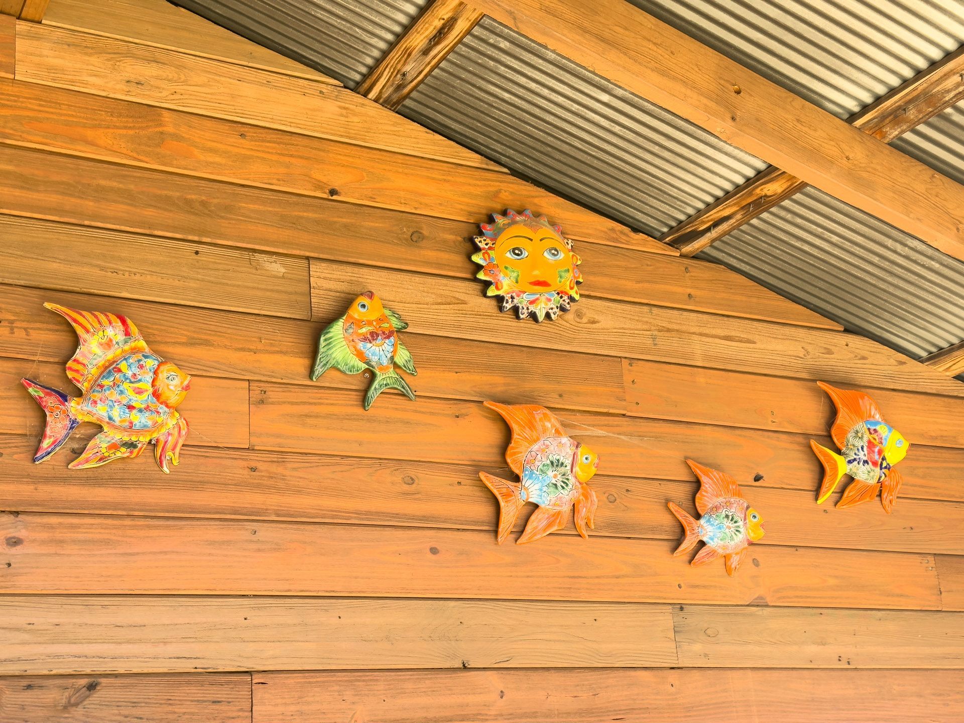 Wooden wall with decorative fish and sun ornaments under a corrugated metal roof.