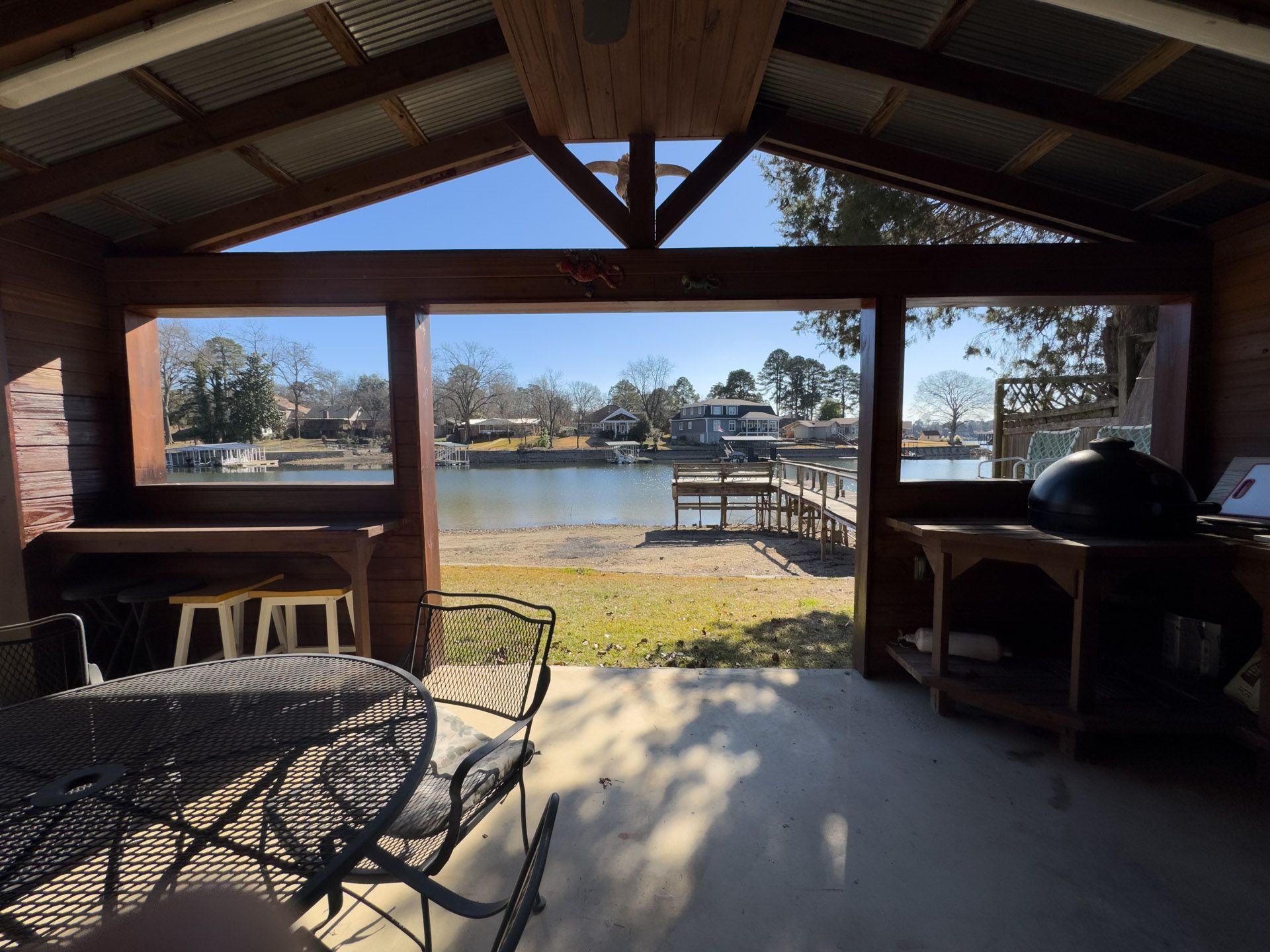 Gazebo overlooking lake with table and grill, blue sky.
