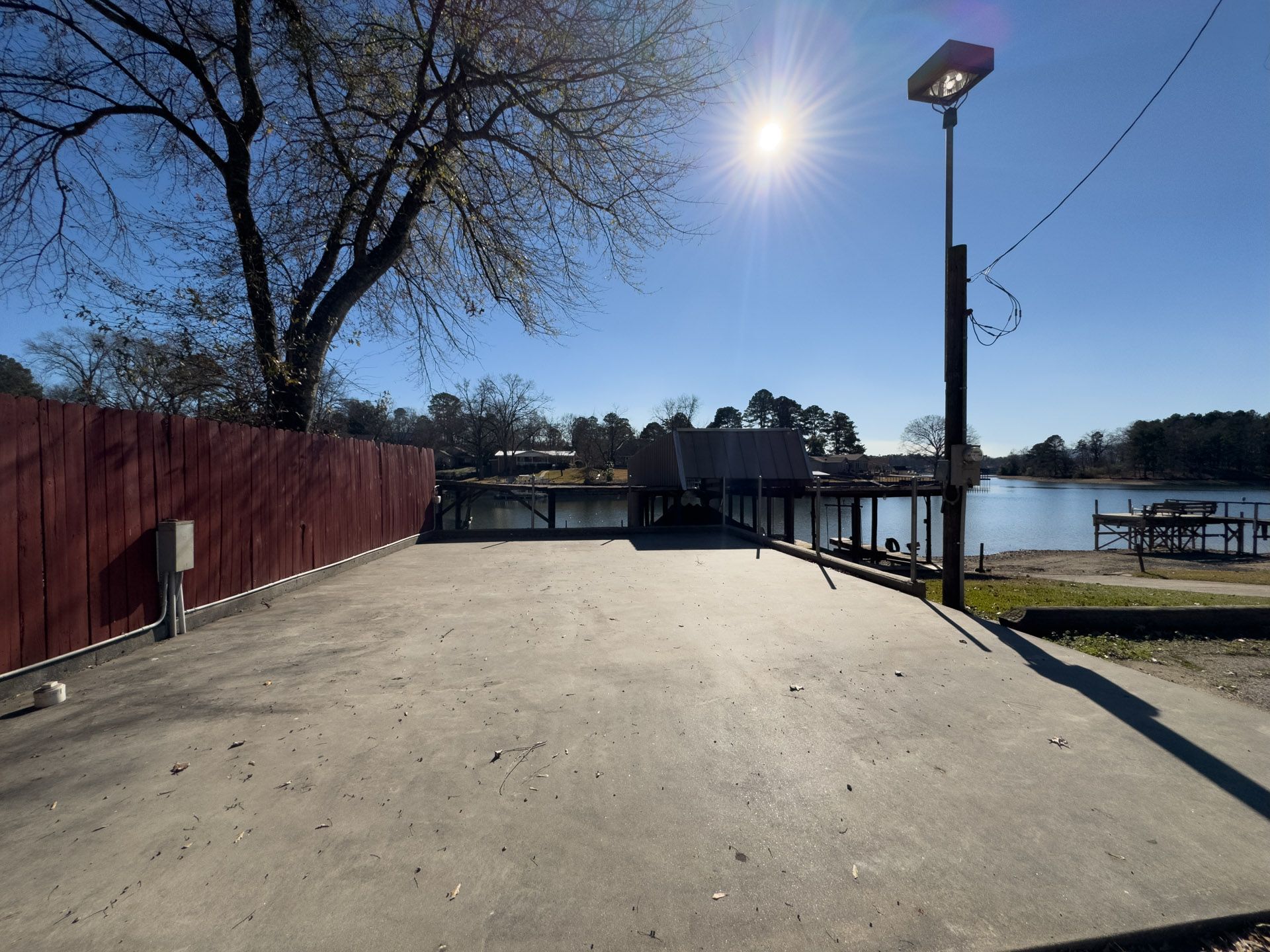 Concrete boat launch leading to a lake, with a wooden fence and dock in the background under a bright, sunny sky.
