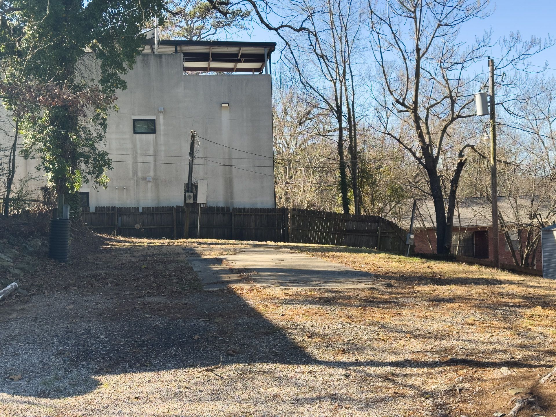 Gravel lot with a tall, light-colored building in the background, surrounded by trees.