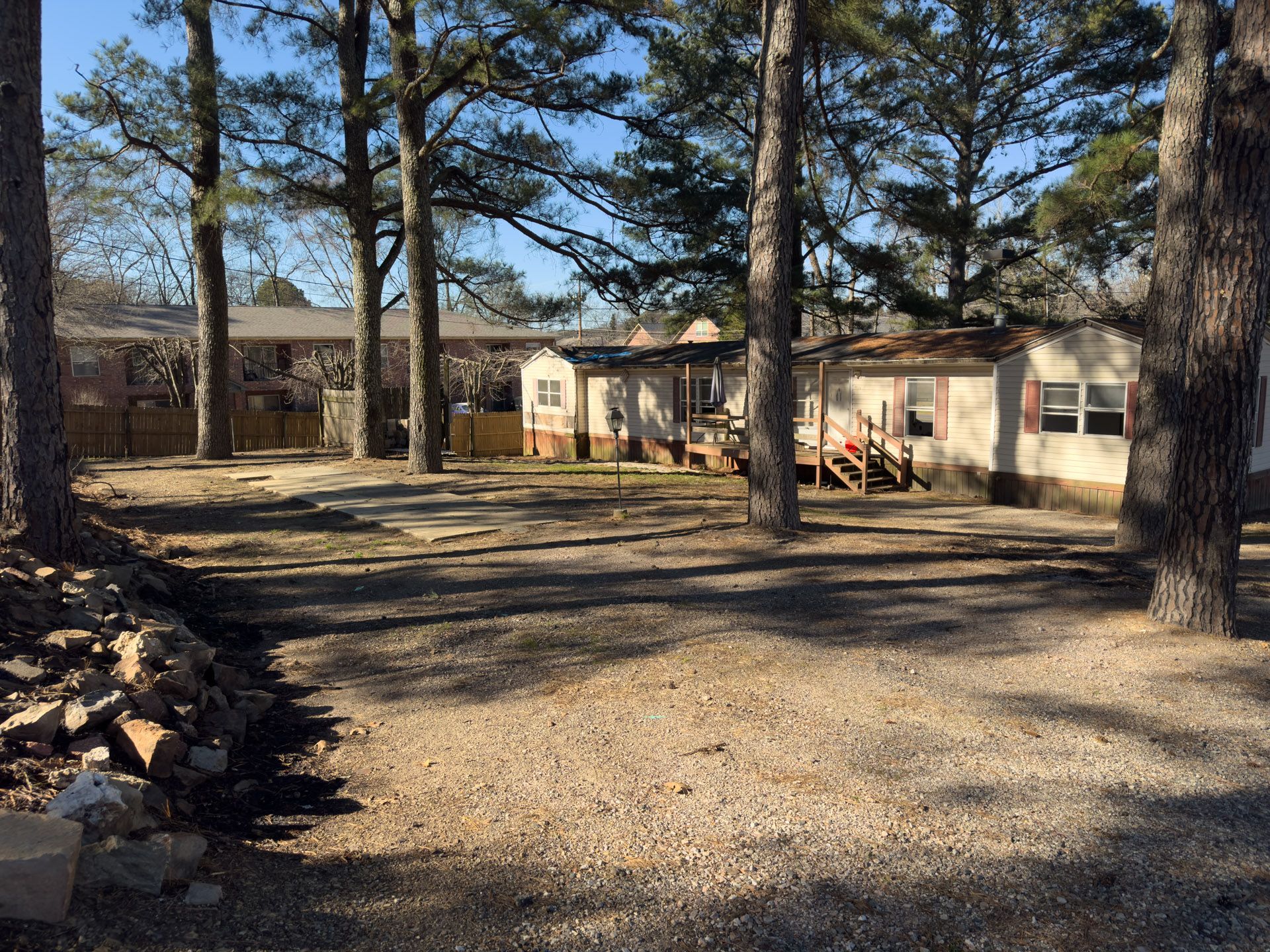 Gravel yard with trees, and mobile homes in the background under a blue sky.