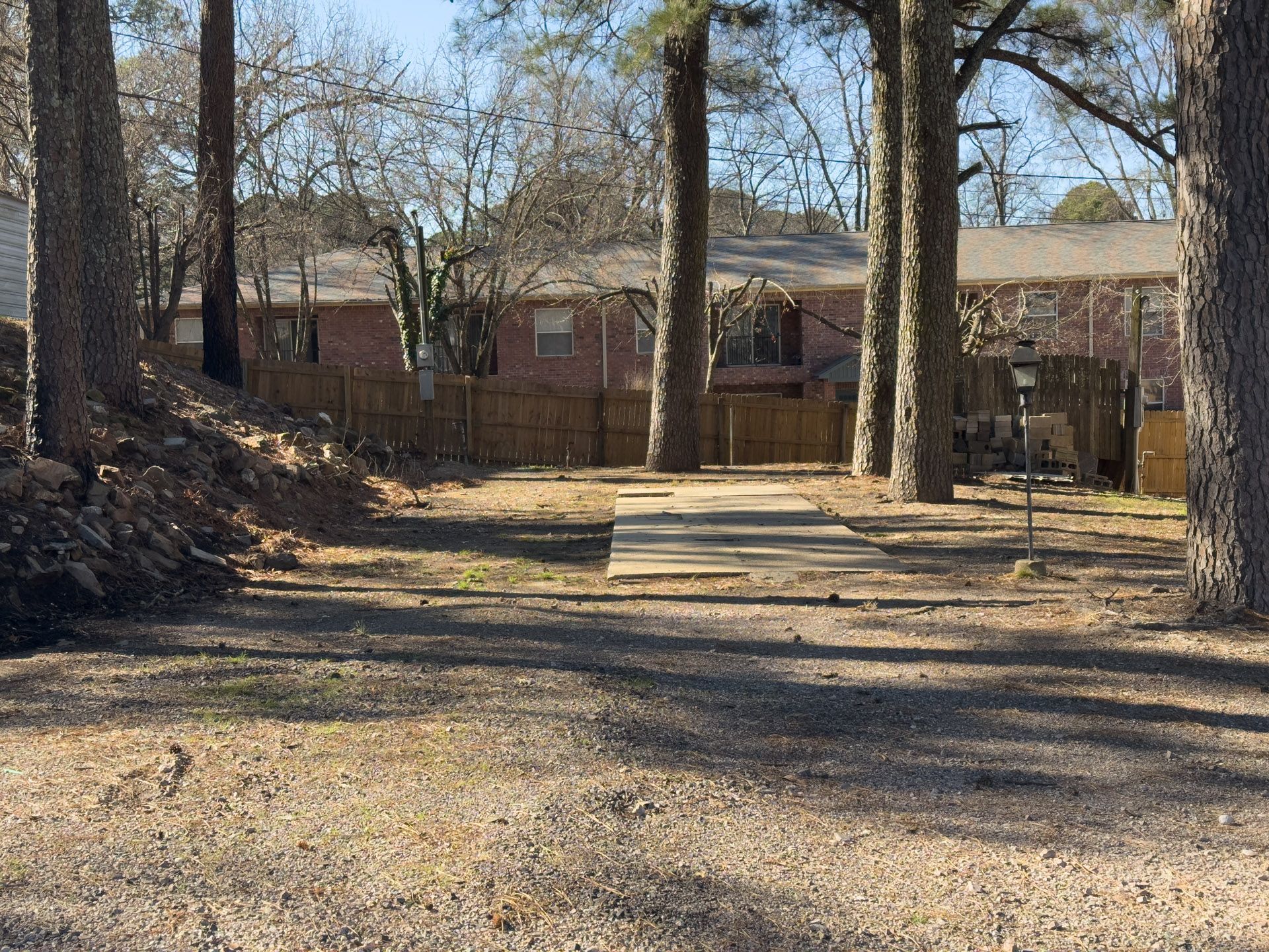 Dirt path leading to a disc golf basket, viewed between trees, with houses in the background.