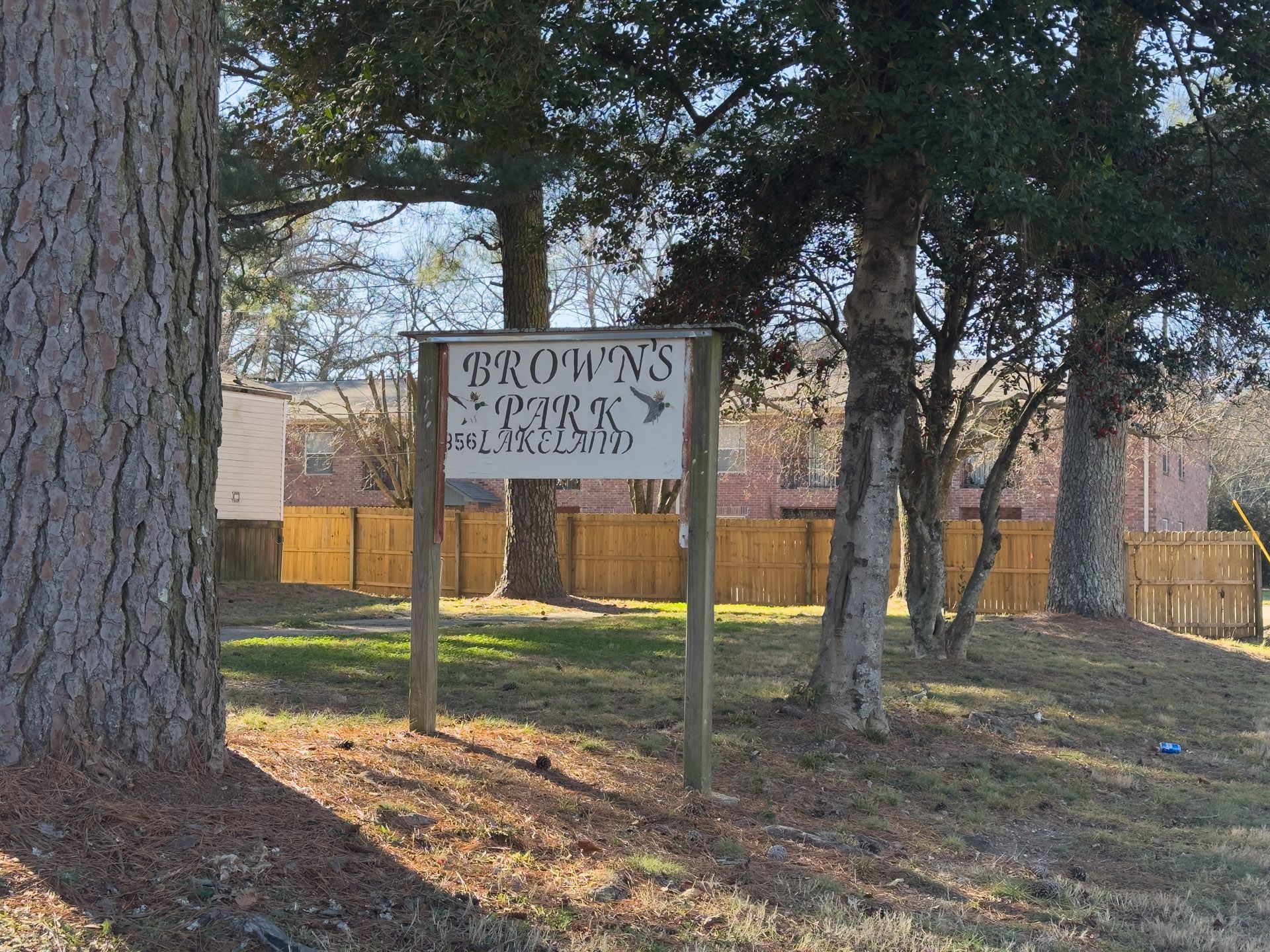 Sign for Brogan's Sporting Goods on grassy area, small trees, and a wooden fence.
