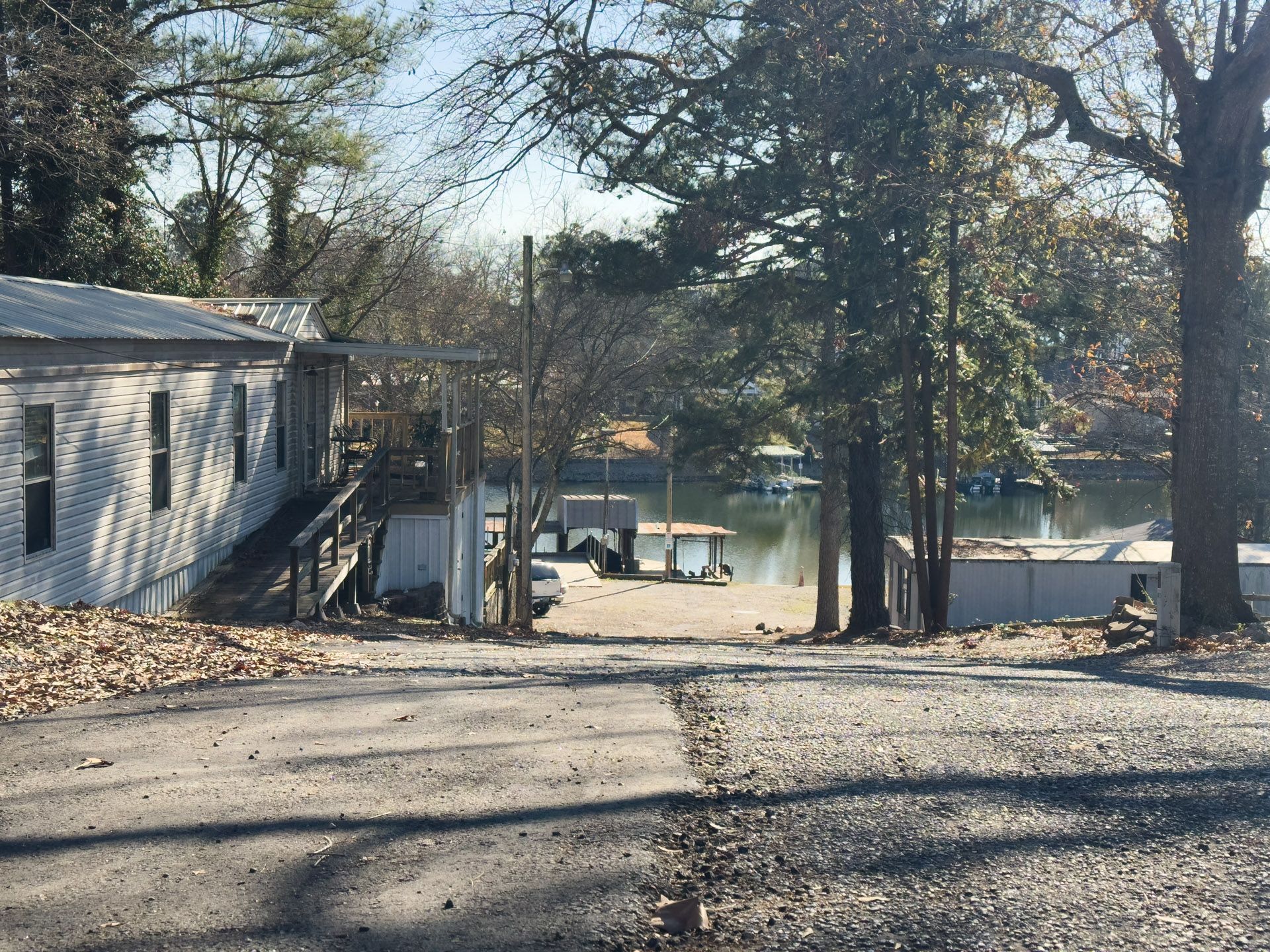 Gravel road leading to a lake with boat docks. Structures on either side. Trees with bare branches.