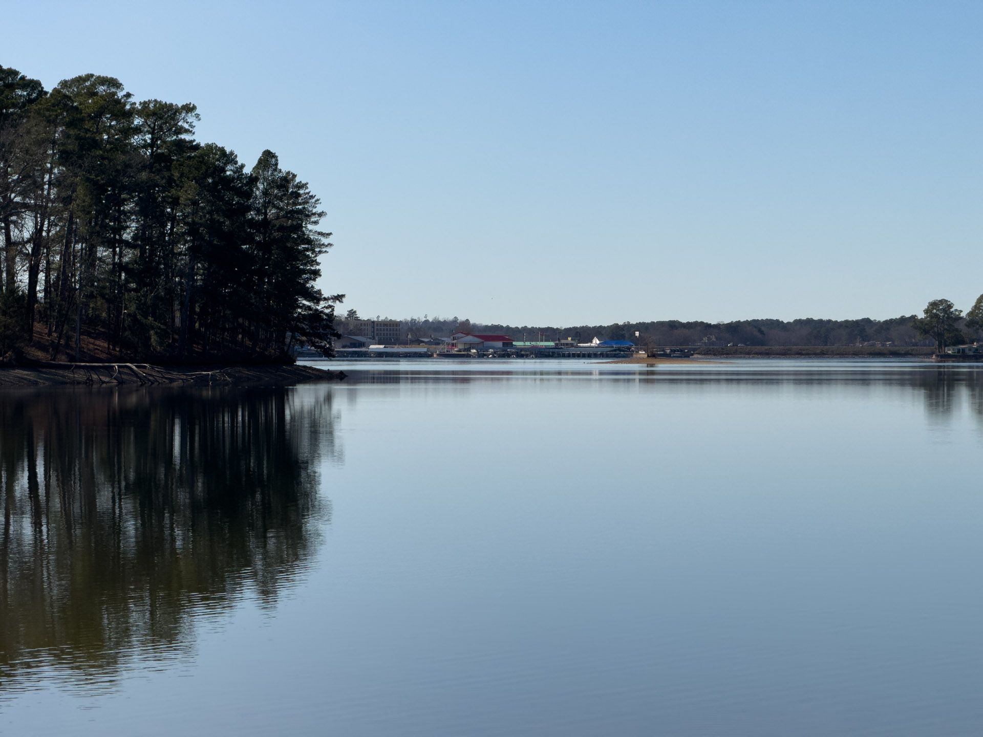 Still water reflecting trees and a distant structure under a clear blue sky.