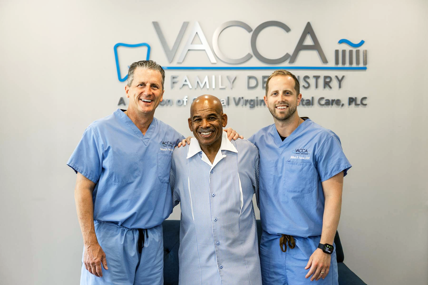 Three men in blue scrubs are posing for a picture with a man in a striped shirt.
