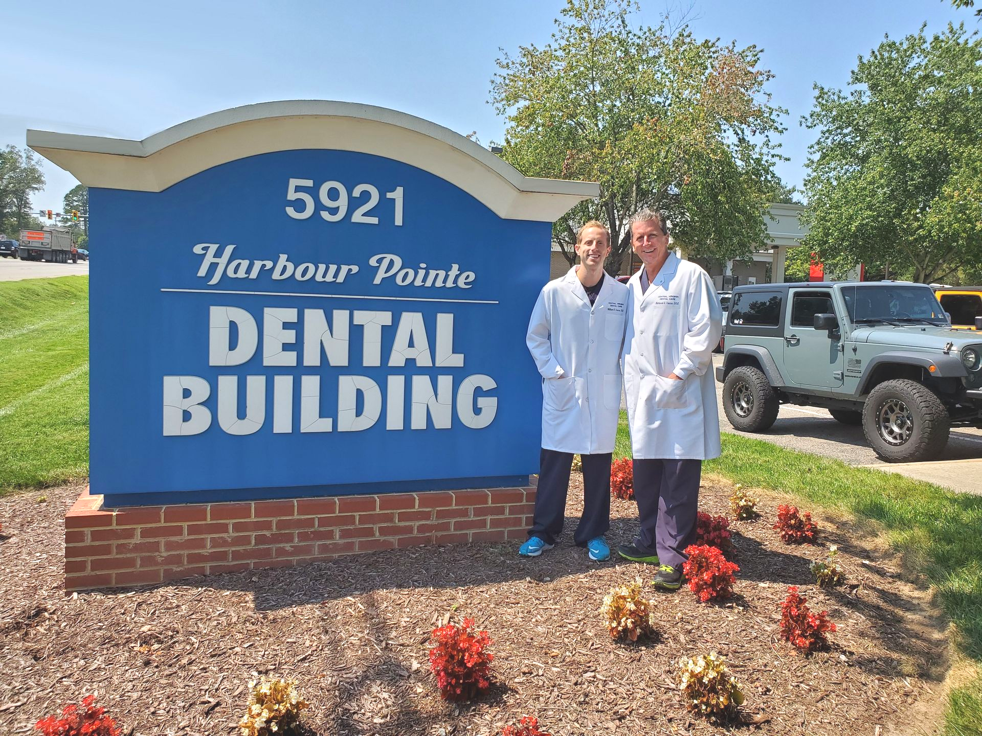Two people in white coats stand by the Harbour Pointe Dental Building sign.